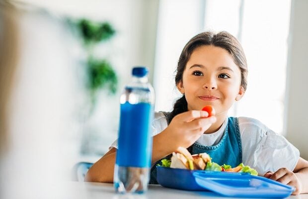 happy little schoolgirl eating lunch at school cafeteria