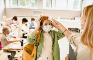 teacher measuring temperature on pupil`s forehead classmate schoolgirl before lesson