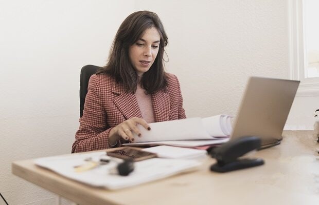 serious woman with documents near laptop at workplace