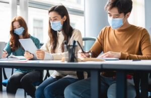 diverse students in masks sitting at desk in classroom