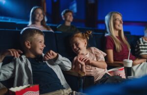 mother with happy small children in the cinema, watching film and laughing.