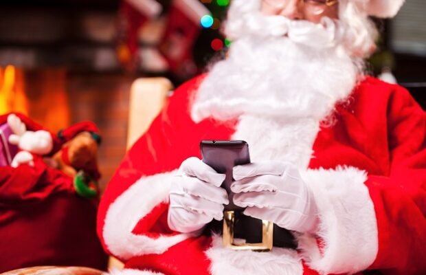 santa claus texting. close up of happy santa claus typing message on the mobile phone and smiling while sitting at his chair