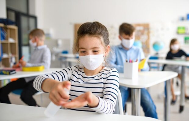 small girl with face mask at school after covid 19 lockdown, disinfecting hands.
