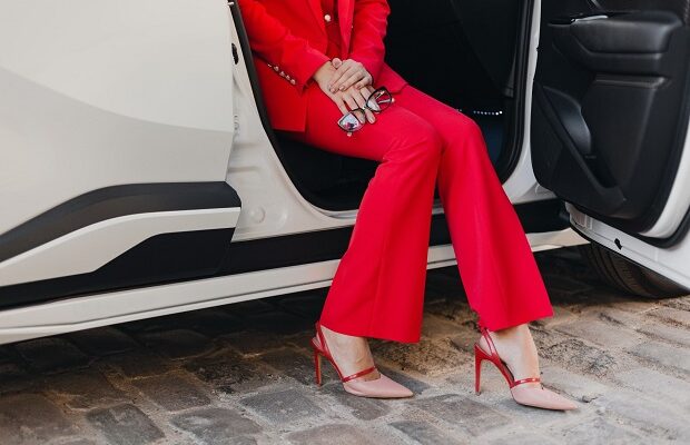 close up legs in heels and hands holding glasses of beautiful sexy rich business woman in red suit posing in white car