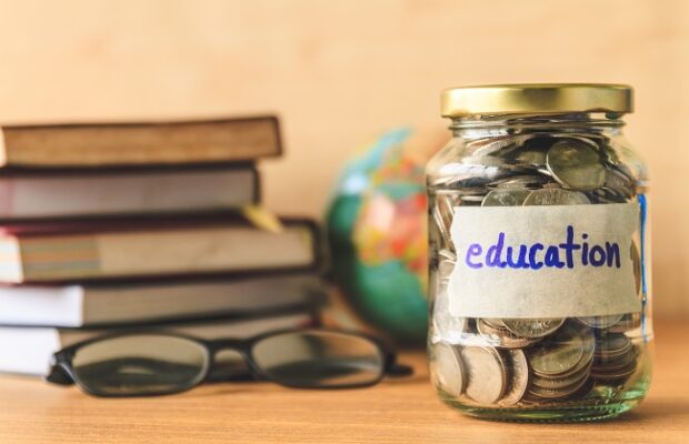 coins in glass jar with education label, books,glasses and globe