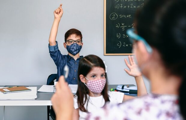 students with masks raising hands at school