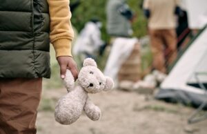 hand of homeless child holding white teddybear