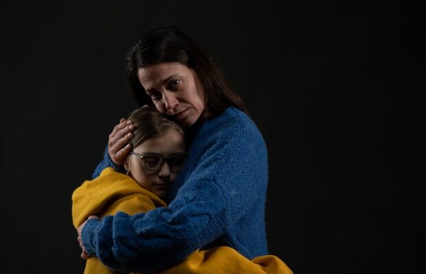sad mother hugging her daughter, both wearing ukrainian national colors on black background.