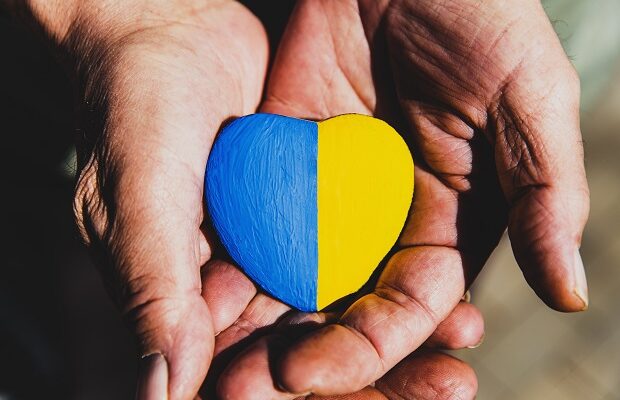 senior man or soldier hands holding heart shape stone painted with ukraine flag