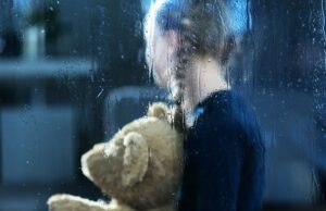 girl with teddy bear behind window covered by rain drops