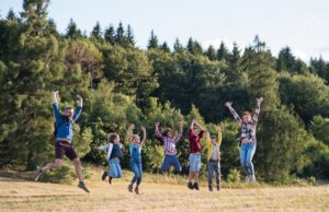 group of school children with teacher on field trip in nature, jumping.