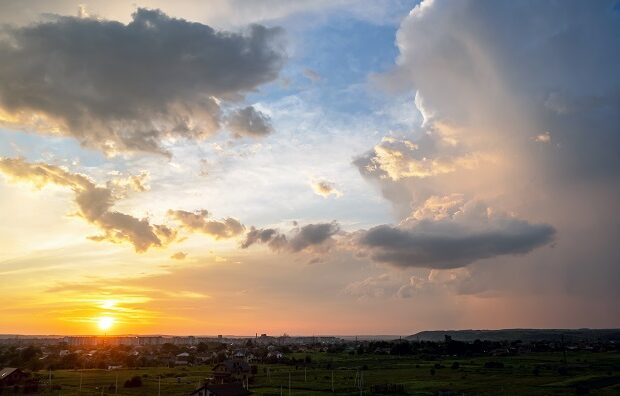 dramatic sunset landscape of rural area with stormy puffy clouds lit by orange setting sun and blue sky.