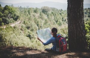 young woman backpacker hiker reading map hiking trip looking awa