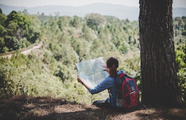 young woman backpacker hiker reading map hiking trip looking awa