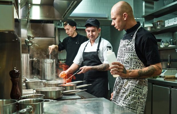 dangerous work. profesional chef teaching his two young trainees how how to flambe food safely. cooking techniques