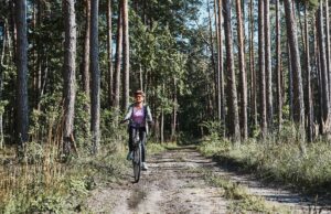 active woman cycling on forest road. female riding bicycle off road route on summer vacation day. woman wearing bicycle helmet and gloves