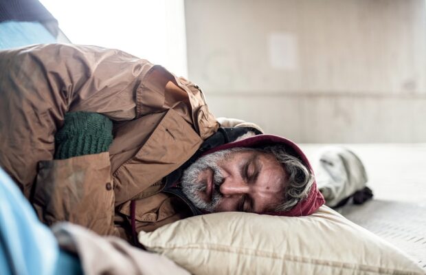 homeless beggar man lying on the ground outdoors in city, sleeping.