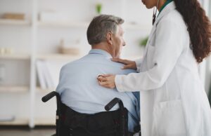 female doctor using stethoscope on older man in wheelchair at home