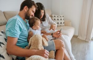 happy parents with baby using smartphone on sofa