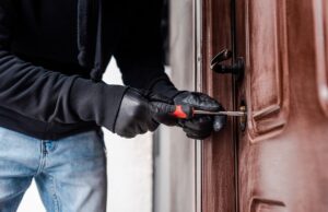 cropped view of housebreaker in leather gloves breaking door lock with screwdriver