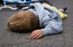 little boy fallen from bicycle and lying still on road after car accident.