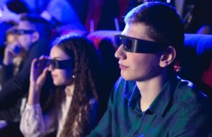 young smiling friends in 3d glasses eating popcorn and watching movie in cinema.