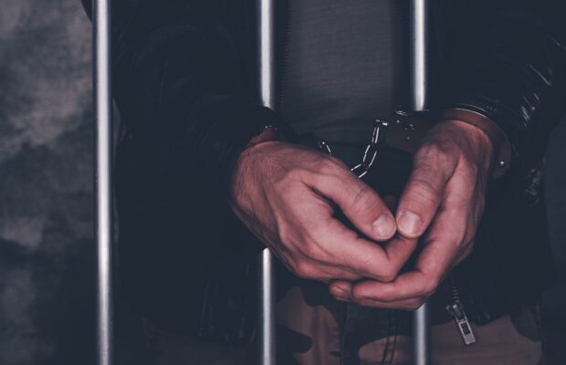 handcuffed man behind prison bars