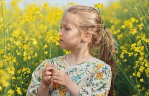 a girl in a dress in a field of rapeseed smelling flowers