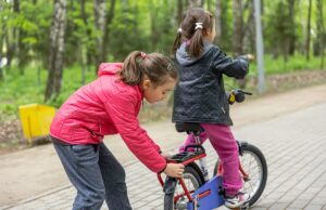 two little girls ride a bike in the park in spring.