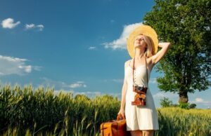 blonde woman with suitcase and camera in wheat field in summer t